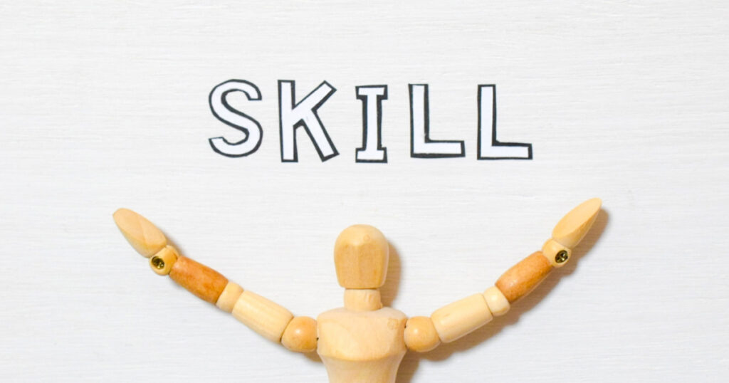 「SKILL」という文字の下で両手を広げる木製人形
