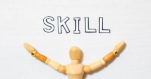 「SKILL」という文字の下で両手を広げる木製人形